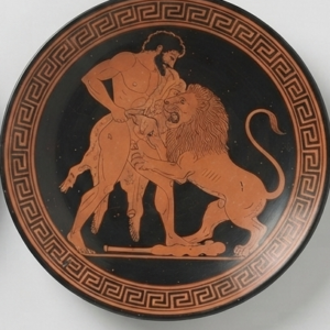 Assiette noire à décor cuivre : Héraclès luttant contre le lion de Némée, frise de méandres.